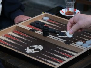 Backgammon in Turkey, shown by a hand moving a white checker on an inlaid wooden board beside a tulip-shaped tea glass