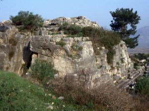 Rock-cut base of the Belevi Mausoleum seen from the southeast with a pine tree and mountains behind it