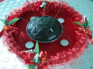 Bowl of henna paste on a red satin tray trimmed with ribbons and flowers, with tea light candles and sparklers, prepared for a Turkish henna night