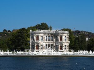 White Küçüksu Pavilion with ornate windows and a carved facade on the shore of the Bosphorus in Istanbul, seen from the water under a blue sky
