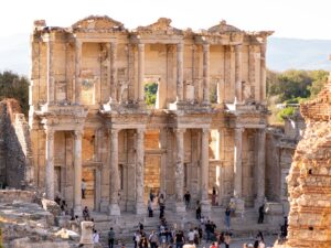 Two-story facade of the Library of Celsus in Ephesus in warm afternoon light, with small groups of visitors on the steps in front of it