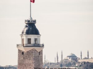 Maiden's Tower on its small island in the Bosphorus, Istanbul, with a Turkish flag on its mast and the domes and minarets of Hagia Sophia on the skyline behind