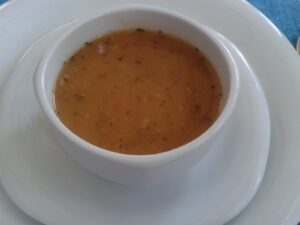 Tarhana soup, a bowl of thick orange-brown soup with flecks of herbs, served in a white cup on a white plate