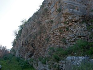 Long stone wall built of large blocks and small rubble stones with green bushes on top at the Ephesus ancient city