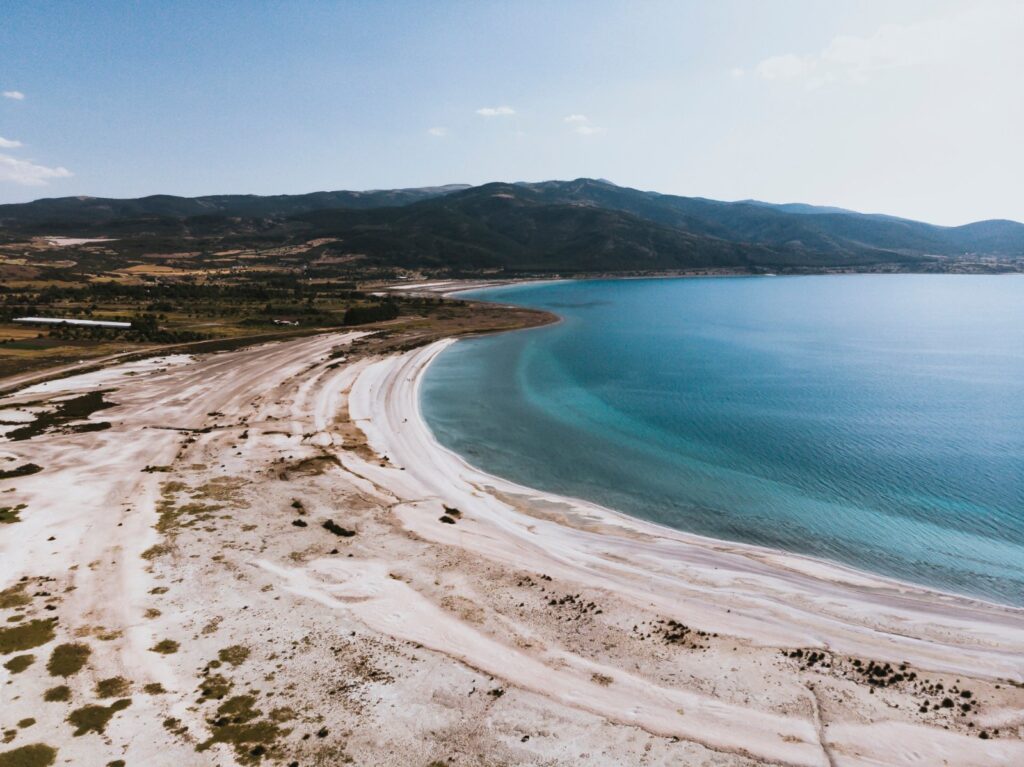 Lake Salda 1 Aerial view of Lake Salda in Burdur Province, with a curved white shore, clear turquoise water and forested mountains under a pale blue sky